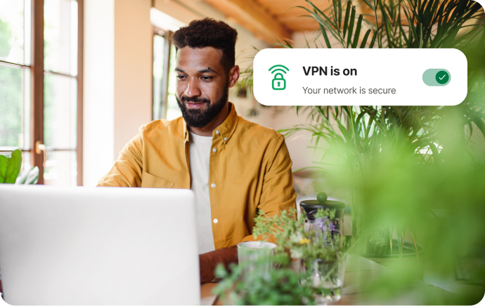 Un bărbat înconjurat de plante care zâmbește spre un laptop